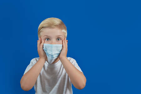 European boy in a medical mask looks right on a blue background