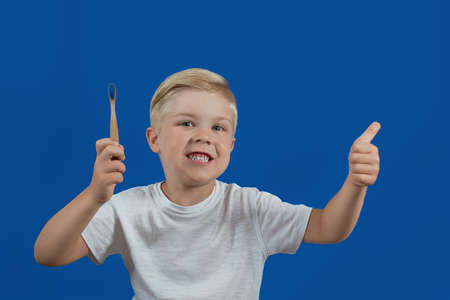 The boy holds a toothbrush with paste and shows thumbs up on a blue backgroundの写真素材