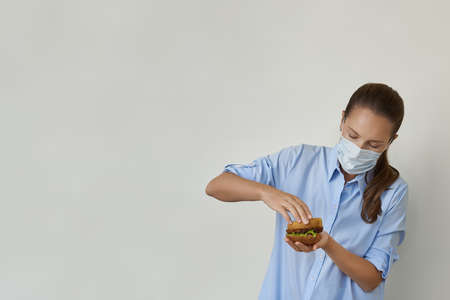 Beautiful young woman cooking vegan burger in protective face mask