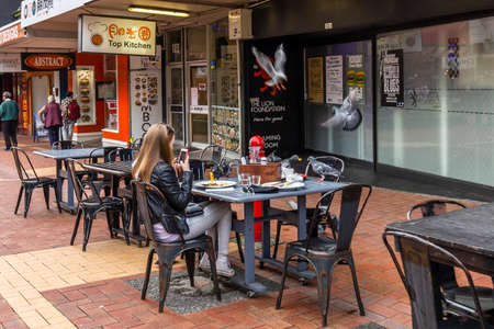 Wellington, New Zealand - August 06, 2018: Woman chasing away some pigeon stealing food from the table in Wellington CBD, New Zealandのeditorial素材