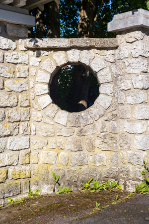 Stone Wall with Circular Opening and Vegetation in Sunlightの写真素材
