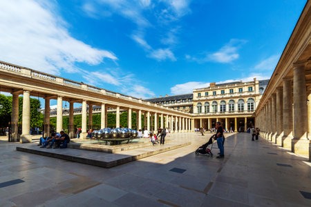 Paris, France - May 19, 2024: Visitors enjoy a peaceful moment in the sunlit courtyard of the Palais Royal in Paris, highlighted by a stunning reflective sculpture and elegant neoclassical architectureのeditorial素材
