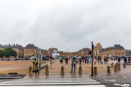 Versailles, France - May 28, 2024: Visitors brave the rain at the entrance of the iconic Palace of Versailles, France, under a blanket of gray skies and umbrellasのeditorial素材