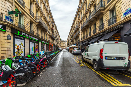 Paris, France - May 27, 2024: A bustling Parisian street lined with rental bikes, shops, and restaurants, captured on a rainy dayのeditorial素材