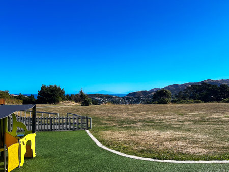 A small playground offers a stunning view of the South Island mountains from the North Island under a clear blue sky in Wellington, New Zealandの写真素材