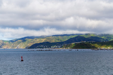 A scenic view of a bay with rolling green mountains and a red buoy, photographed in Wellington, New Zealandの写真素材