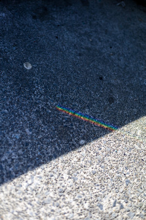 A tiny rainbow glimmers on rough concrete, a delicate play of light and shadowの写真素材