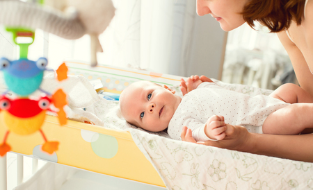 Mother gently care of baby on the changing table at homeの写真素材
