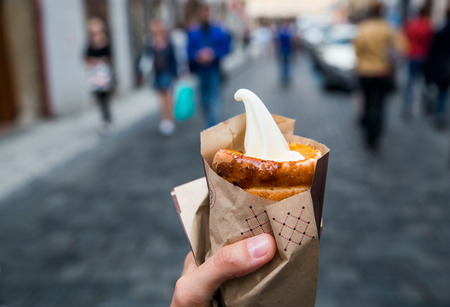 Tourist holds in hand Trdlo or Trdelnik with ice-cream on the background of city tourist streets of Czech (Prague). Fresh Appetizing Trdlo or Trdelnik - Traditional National Czech Sweet Pastry Dough.の写真素材
