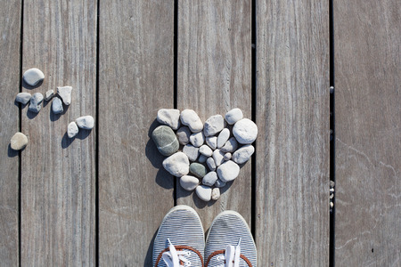 Shape of heart made with stones with shoes on the wooden planks of pier background. Love, Zen, Balance, Life Concept.の写真素材