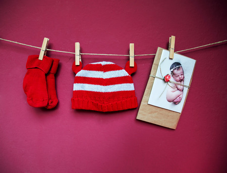 Baby child clothes (hat and socks) and greeting card with cutest newborn baby hanging on the clothesline on a textured wall background with copy space. Baby concept background.の写真素材