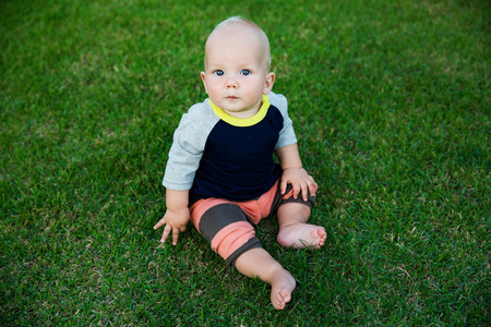 Happy adorable baby boy sitting on the grass and laughing in summer day. Happy smile, 8 months old. Child in trendy and cute clothesの写真素材