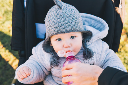 Portrait of a cute baby on a walk outdoors. Child sits in a stroller and drinking water from bottle.の写真素材