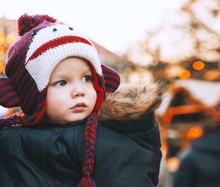 Portrait of child in a funny hat spend winter holidays with family in the old town of Klagenfurt, Austria. Holidays, Christmas, Family concept. Child at winter outdoor among Christmas decorationsの写真素材