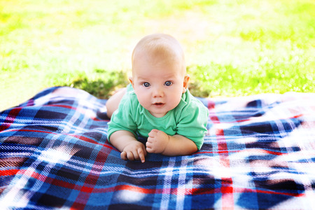 Cute child baby boy lying on blanket in summer day on nature. Happy smile, 6 months old, outdoor. Family picnic in a park.の写真素材