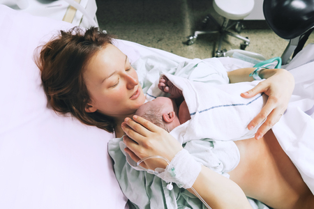 Mother holding her newborn baby child after labor in a hospital. Mother giving birth to a baby boy. Parent and infant first moments of bonding.の写真素材