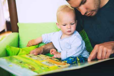 A little boy is reading a book with his father in a home interiors. Father and son spend time together. Family, Childhood concept.の写真素材