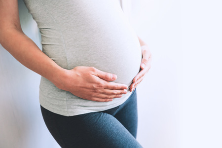 Pregnant woman holds hands on belly at home interiors. Pregnancy, parenthood, preparation and...