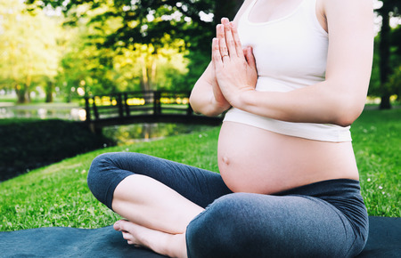 Close-up of pregnant woman meditating while sitting in lotus position. Sport, fitness, healthy life during pregnancy. Beautiful pregnant woman doing prenatal yoga on nature outdoors.の写真素材