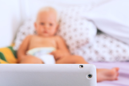 Toddler boy watching cartoons on tablet. Focus on foreground with computer device and blurred looking baby on the background. Child with tablet - concept photo.の写真素材