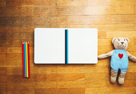 Child or baby play set with empty book or notepad, colored pencils, teddy bear. Back to school, education concept. Kindergarten or preschool background.の写真素材