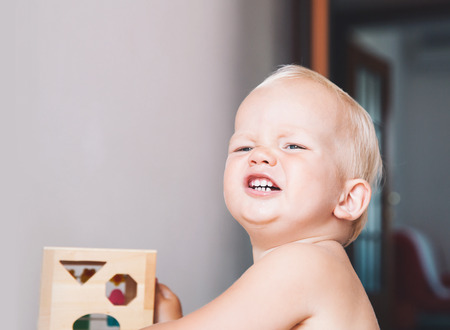 Cute toddler frowns and expresses disagreement on his face. Adorable baby boy makes a funny serious disagrees displeased face at home interiors. Portrait of an angry child. Early development of babyの写真素材
