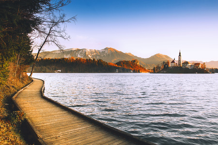 Amazing view on Bled Lake on sunrise with wooden promenade. Island with Catholic Church in Bled Lake with Castle and Mountains. Morning on the lake at dawn. Autumn, Winter in Slovenia, Europe.の写真素材