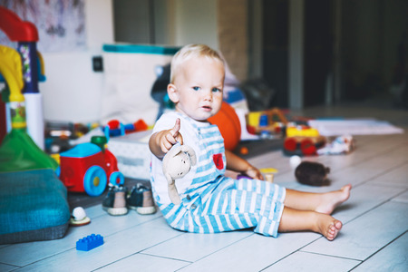 ?hild plays with soft toys at home with many colorful toys on background. Cute little boy with teddy bear pointed in camera. Family concept background.の写真素材