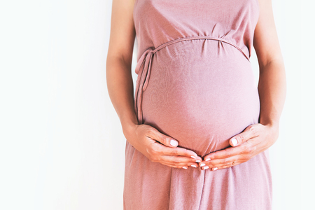 Pregnant woman in dress holds hands on belly on a white background. Pregnancy, maternity,...