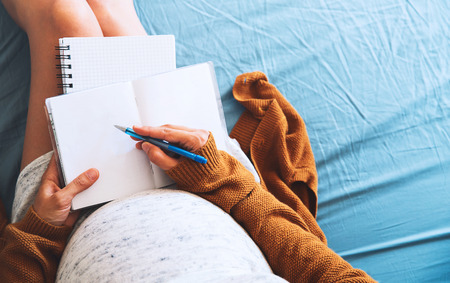 Pregnant woman makes notes and looking at medical documents. Concept of pregnancy, health care,...