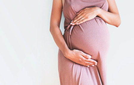 Pregnant woman in dress holds hands on belly on a white background. Pregnancy, maternity,...