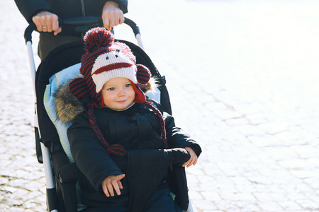 Cute smiling child boy in a funny hat in stroller spending winter holidays with family at the...