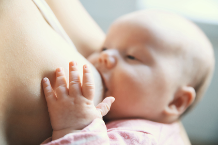 Baby eating mother's milk. Mother breastfeeding baby. Young woman nursing and feeding baby. Concept of lactation infant. Focus on the little child's pen, blurred background. の写真素材