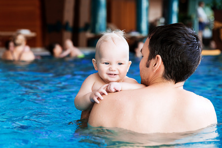 Father teaching baby to swim. Portrait of a charming 11 months child in the classroom in a swimming pool. Healthy Family Life.の写真素材