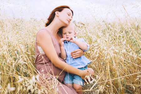 Beautiful pregnant woman and her cute toddler son having fun on wheat field with haystacks at summer day on nature, outdoors. Young mother waiting of a second baby. Pregnancy and family image. Mom and childの写真素材