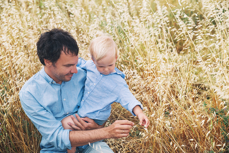 Happy father and son. Family background. Dad and his little cute kid boy playing and hugging on wheat field with haystacks at summer day on nature, outdoors. Concept of trust, confidence, loveの写真素材