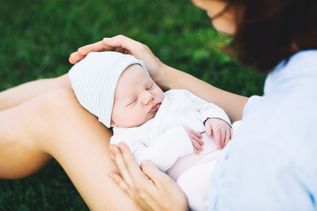 Loving mother with her newborn baby on her arms. Beautiful mom with a cute sleeping new born child on nature outdoors. Baby's first week of life. Happy maternity and harmonious family.の写真素材