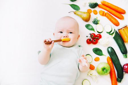 Healthy child nutrition, food background, top view. Baby 8 months old surrounded with different fresh fruits and vegetables on white background. Baby first solid feedingの写真素材