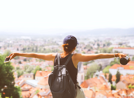 Woman tourist delights amazing panoramic view with red roofs of Ljubljana from Castle. Girl traveler with backpack discovers Slovenia. Springtime or Summer in Europe. Travel and Vacationの写真素材