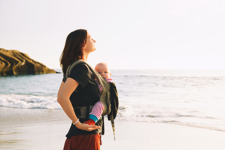 Baby and mother on sea at summer day. Happy family walking on nature outdoors. Child in a carrier backpack. Woman and her baby on coastline ocean on the island of Tenerife, Spain. Travel Europeの写真素材