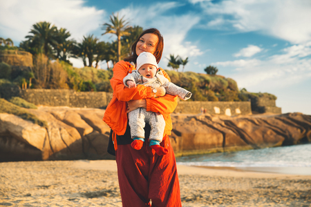 Family holiday on Tenerife, Spain, Europe. Mother and baby outdoors on ocean. Portrait travel tourists - mom with child. Positive human emotions, active lifestyles. Happy young family on sea beachの写真素材