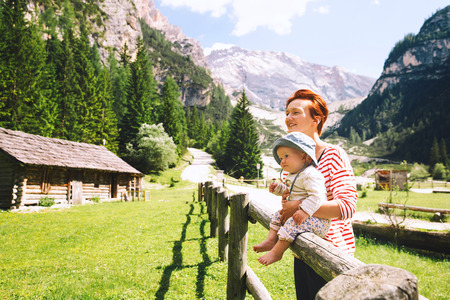 Mother and baby with mountains on a background. Family spend summer holiday in Dolomites, South Tyrol, Italy, Europe. Woman and child on nature in the countryside in the Alpine villageの写真素材