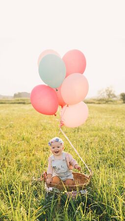 Baby girl in wicker basket with pink balloons in sunlight at summertime. Happy child on nature....