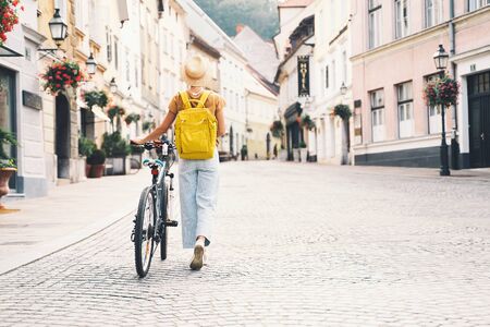 Travel Slovenia, Europe. Young girl with backpack and urban bicycle in old street in historical center of Ljubljana. Traveler woman explores sights of european city. Local living in Ljubljana.の写真素材