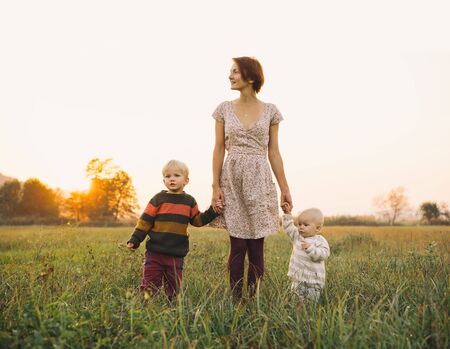 Young mother with children in sunlight at sunset on nature outdoors. Parents and kids in meadow in...