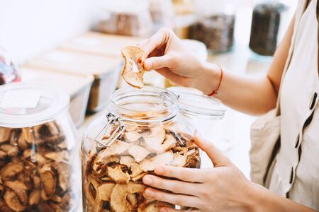 Woman with glass jars buying dried berries and fruits in zero waste shop. Sustainable shopping in...