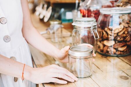 Woman in white linen dress with empty glass jar buying in sustainable plastic free grocery store....