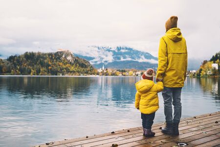 Family Travel Europe. Mother and child in yellow raincoats looking at Bled Lake. Autumn or Winter in Slovenia. View on Island with Church on Bled Lake with Castle and Mountains in Nature Background.の写真素材