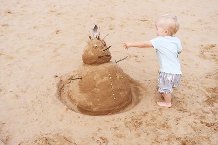 Little girl playing with New Year or Merry Christmas sandy snowman on tropical ocean sand beach. Child on sea coast. Family holiday on Tenerife, Spain. Winter vacation in warm countries.の写真素材