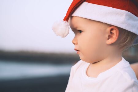 Little girl in red santa hat on ocean coast. Family holiday on Tenerife, Spain. Child playing on black volcanic sand beach. New Year or Merry Christmas, winter vacation in warm countries.の写真素材